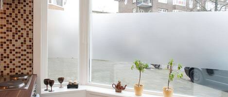 Eine Küche mit Fensterblick auf eine Straße, einer gefliesten Rückwand und einem kleinen Blumentopf auf der Fensterbank.