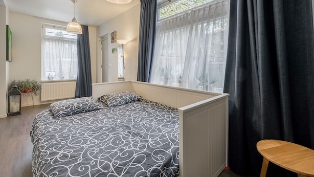 A bedroom with a large bed, a window with curtains, a bedside table, and a hanging light fixture. - Bos en Lommer Apartments (Amsterdam)