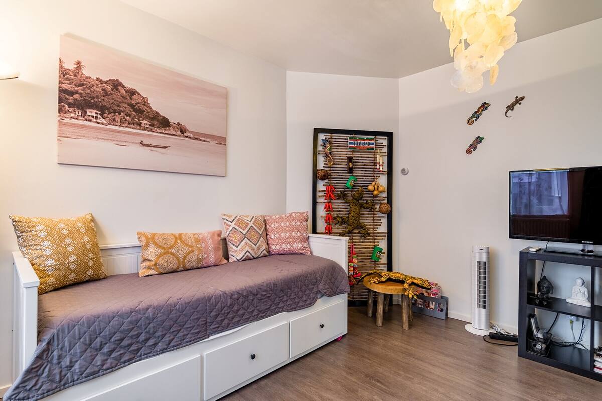 Quarto com cama, TV, prateleira na parede e pintura de uma paisagem praiana.