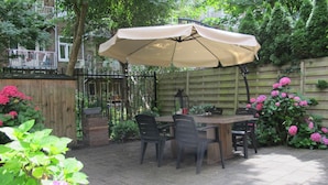 An outdoor patio with a table and chairs, a large umbrella, and a wooden fence. - Bos en Lommer Apartments (Amsterdam)