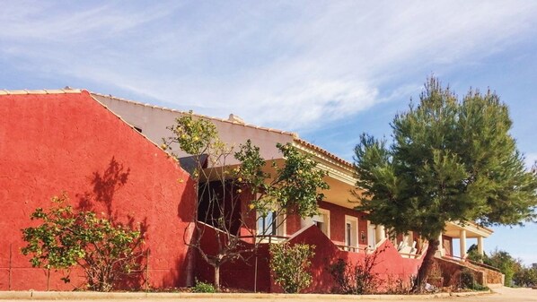 Un edificio con fachada roja, un balcón y un árbol grande en su parte frontal.