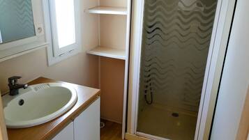 Un baño con lavamanos blanco, espejo, ducha con puerta de vidrio ondulado y encimera de madera.