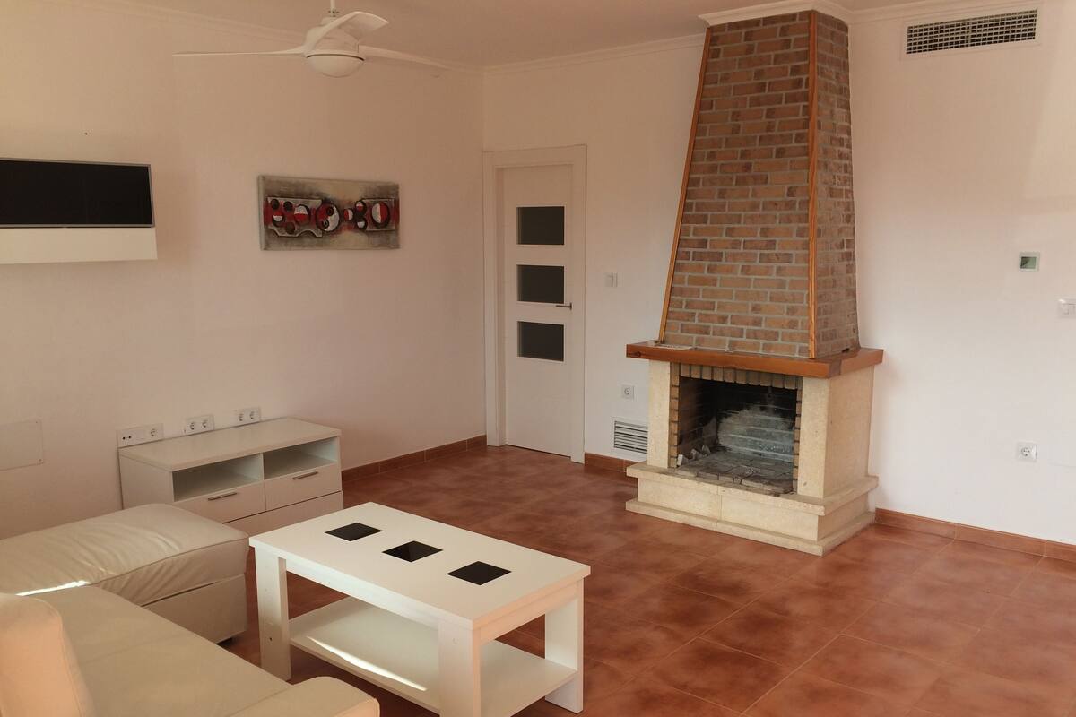 A living room with a sofa, a white coffee table, a fireplace, and a TV mounted on the wall.