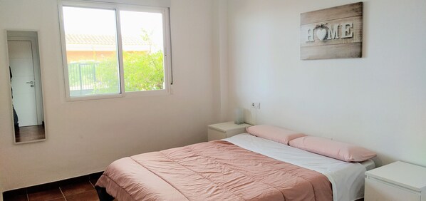 A bedroom with a bed, a nightstand, a bedside table, a window, and a mirror. - Espacio Finca Alegría (Cartagena)