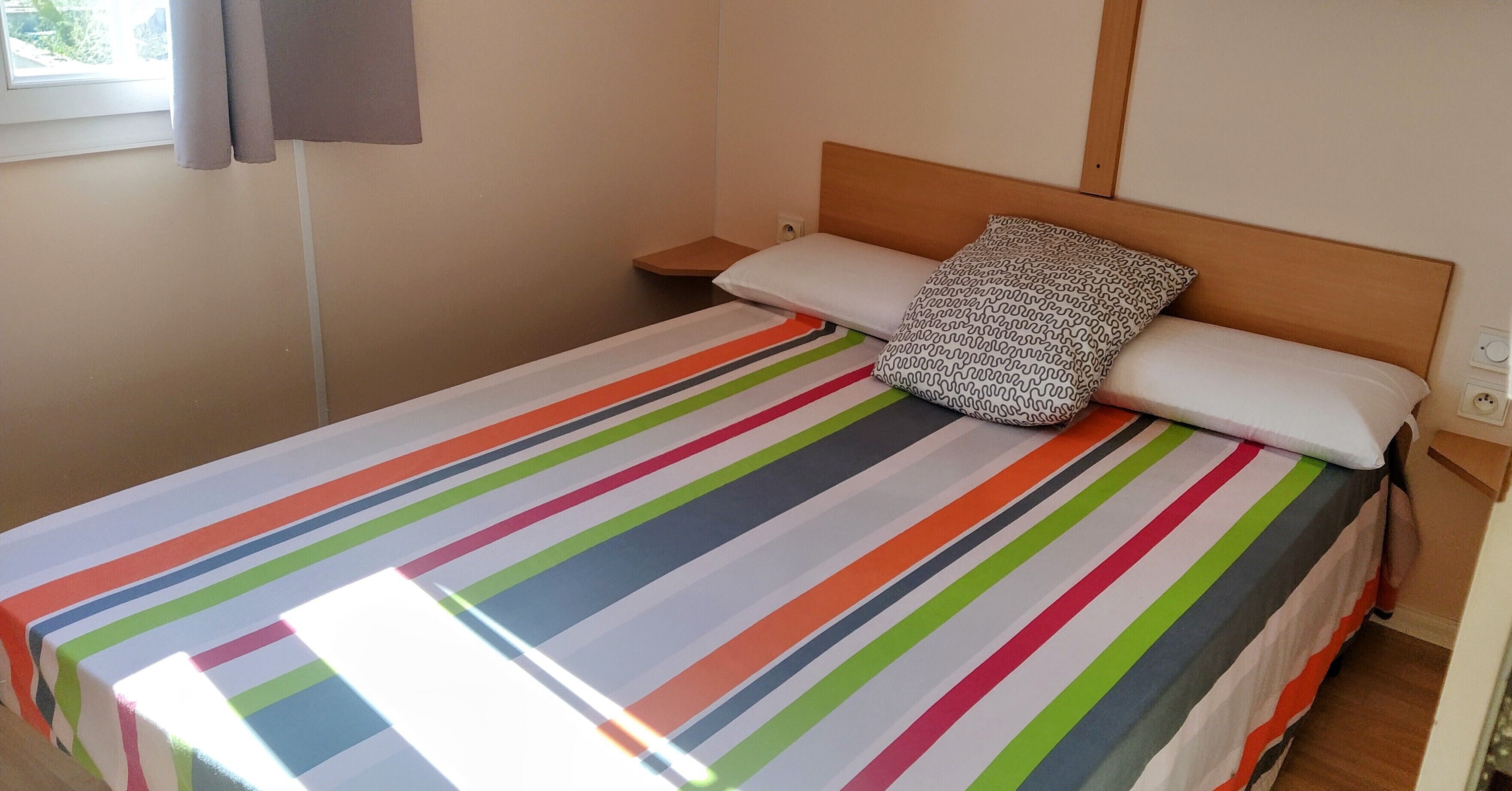 A bed with a striped bedspread, a pillow, and a wooden headboard.