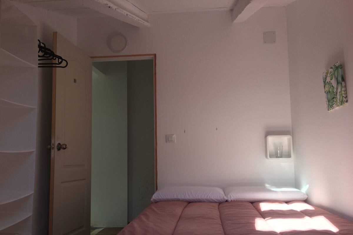 A bedroom with a bed, a door, a wall-mounted light, and a small window.