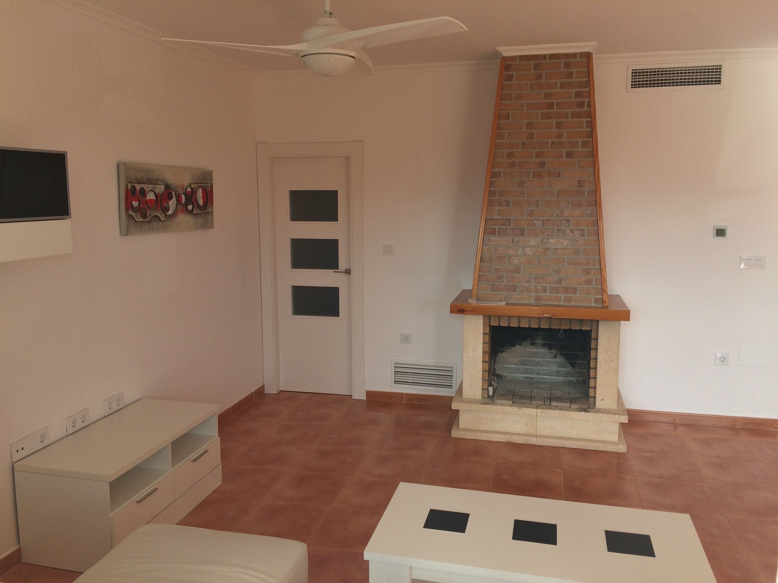 Una sala de estar con chimenea, ventilador de techo y puerta con paneles de vidrio esmerilado.