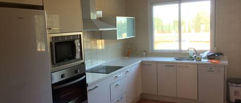 A kitchen with white cabinets, a microwave, an oven, a dishwasher, a window, and a ceiling fan.