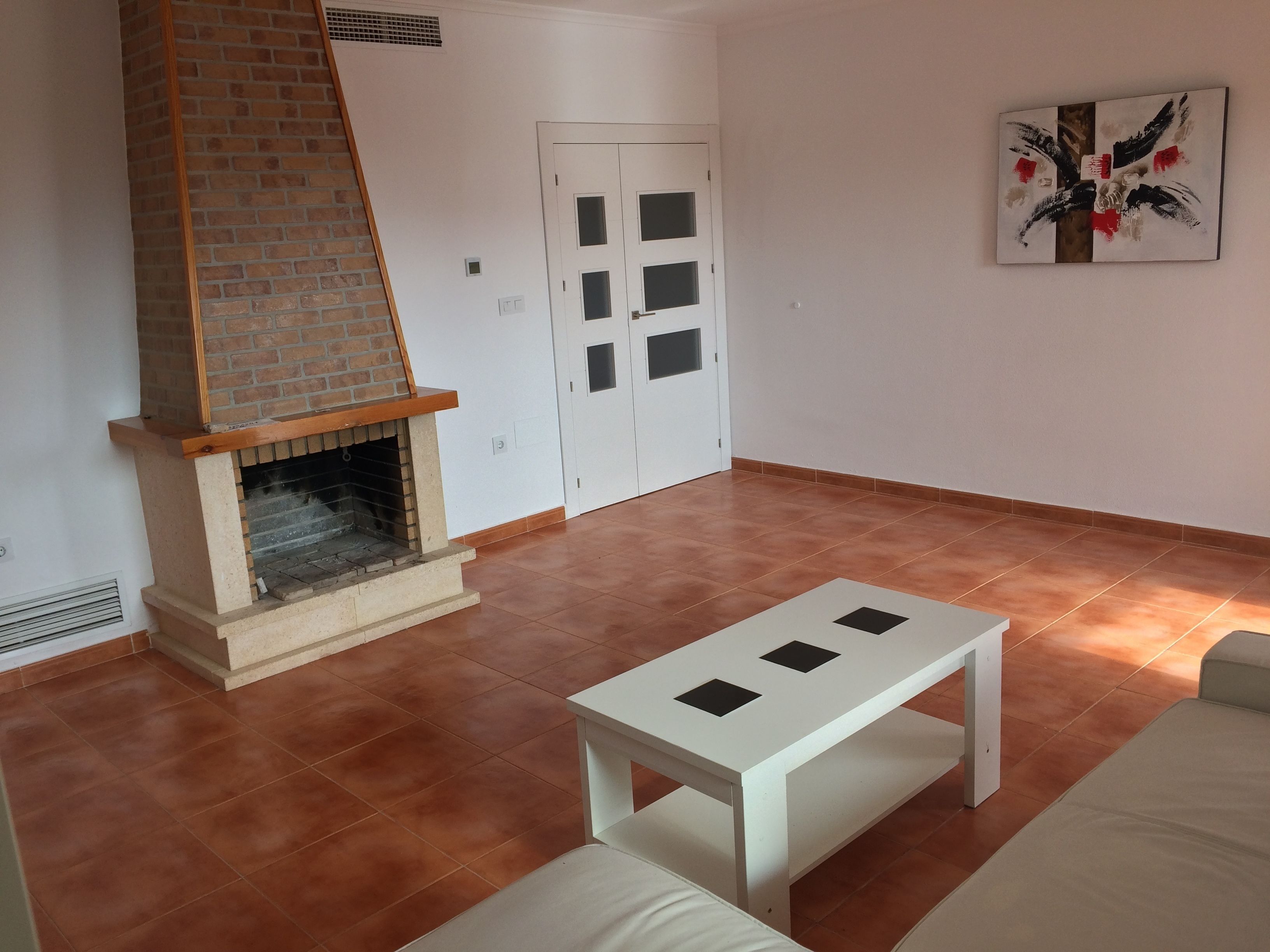 A living room with a fireplace, a white door, and a painting on the wall.