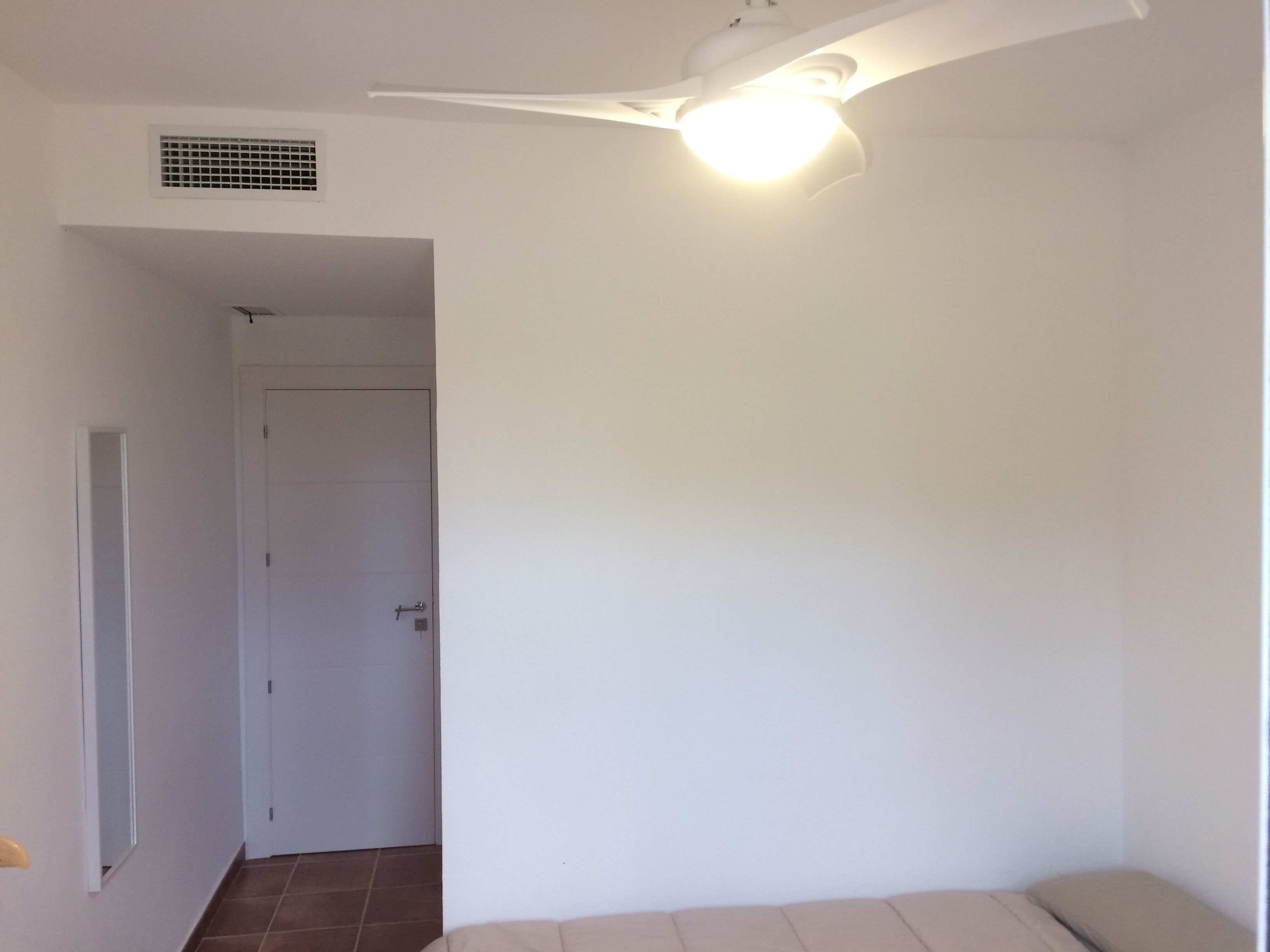 Una habitación con cama, una puerta y un ventilador de techo.