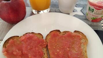 A breakfast plate with toast topped with tomato spread, a glass of orange juice, a cup of coffee, a whole apple, and a container of yogurt.