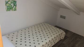 Quarto pequeno com uma cama de solteiro, colcha com padrão de estrelas, travesseiro branco e uma pequena planta na parede.