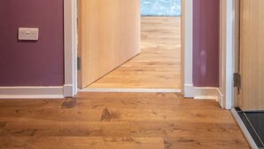 A hallway with a wooden door leading to a room with a blue sofa and a small table.