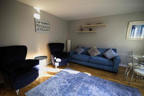 Un salon avec un canapé bleu, deux fauteuils, une petite table ronde et un tapis bleu à motifs.