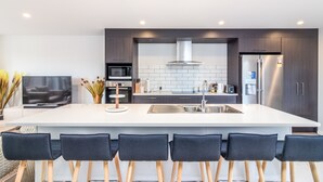 A modern kitchen with a large island, dark cabinets, stainless steel appliances, and a flat-screen TV. - Restful in Riccarton - Christchurch (Christchurch)
