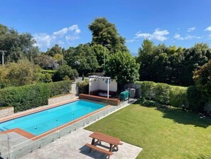 Piscina retangular com revestimento cerâmico, rodeada por um gramado bem cuidado e vegetação densa.