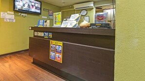 A reception desk with a clock, a television mounted on the wall, and various informational posters. - Juru Hotel (Simpang Ampat)