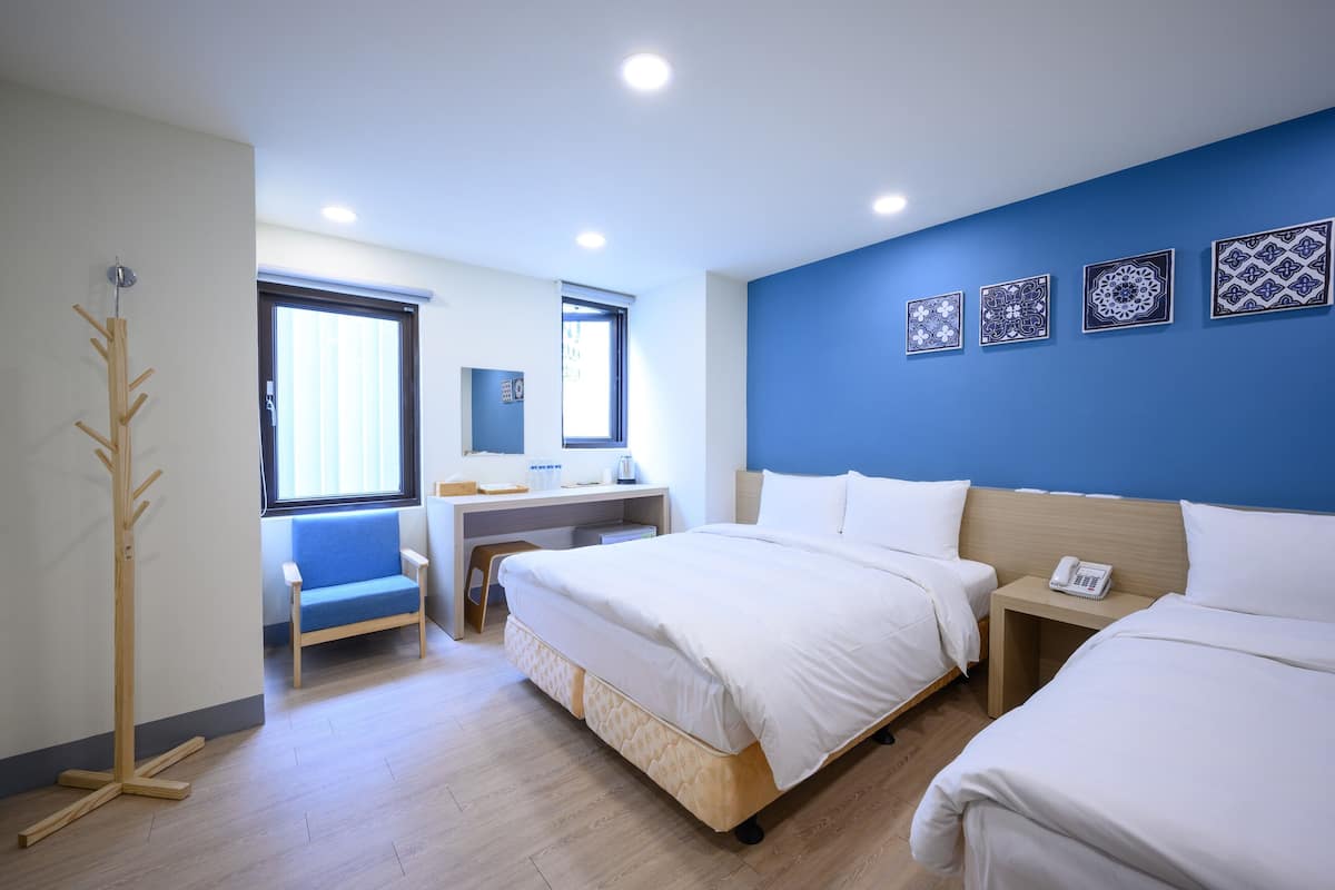 A hotel room with two beds, a desk, a chair, and a coat rack.