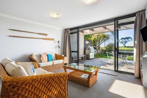 A modern living room with a glass coffee table, wicker furniture, and a view of the outdoors.