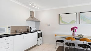Una cocina compacta con armarios blancos, microondas, cocina y pileta. Hay dos mapas enmarcados en la pared y un florero con flores sobre la mesa.