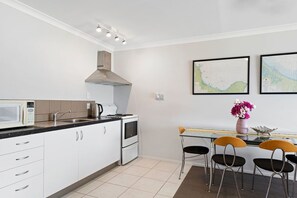 Una cocina compacta con armarios blancos, microondas, cocina y pileta. Hay dos mapas enmarcados en la pared y un florero con flores sobre la mesa.