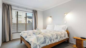 A neatly made bed with a patterned bedspread, a wooden headboard, and a bedside table with a lamp.