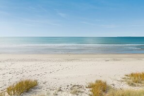 Een zanderig strand met zachte golven, heldere lucht en schaarse begroeiing.
