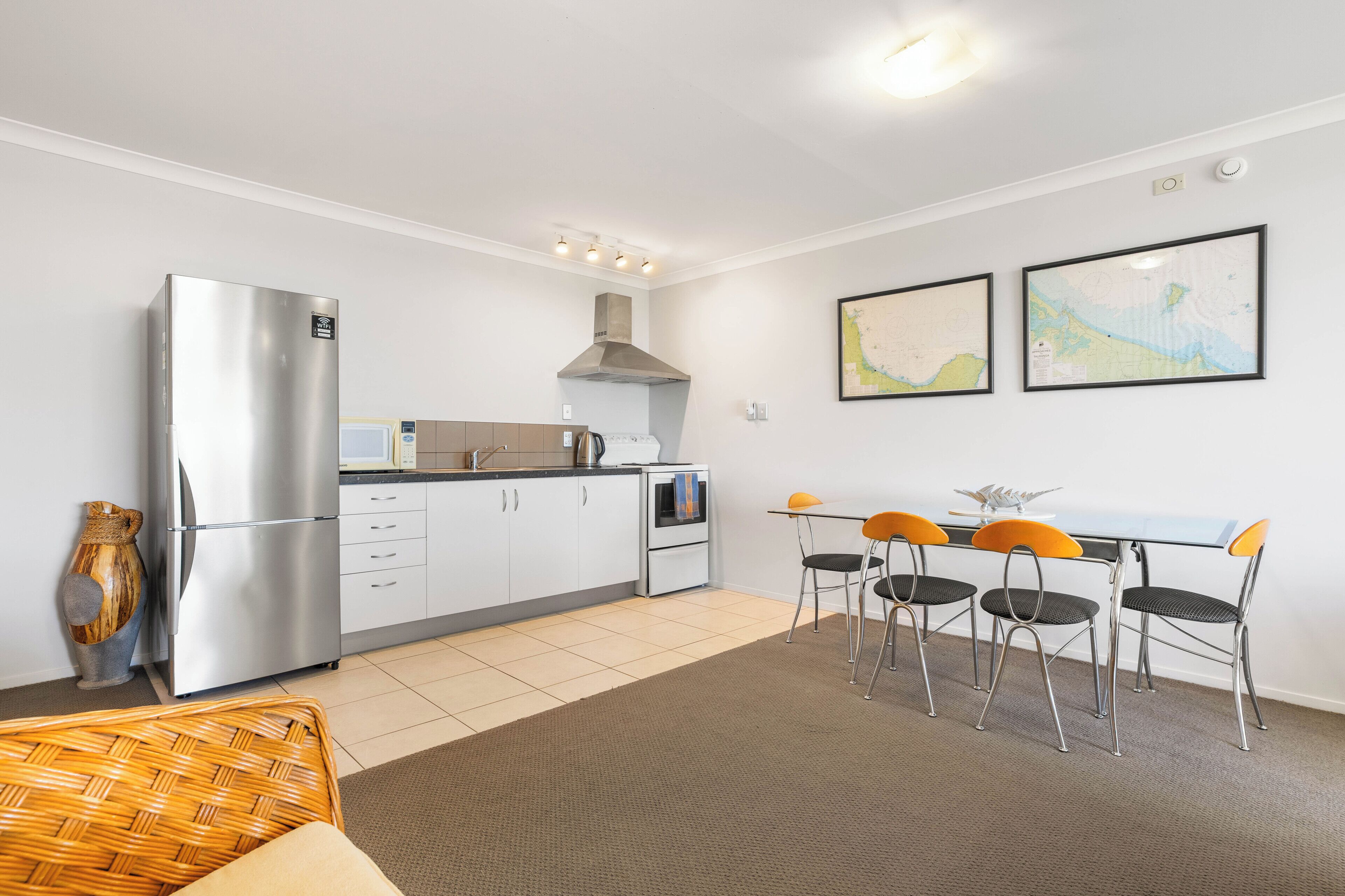 A compact kitchen with a refrigerator, microwave, and stove, a dining area with a table and chairs, and two framed maps on the wall.