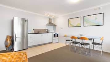 A compact kitchen with a refrigerator, microwave, and stove, a dining area with a table and chairs, and two framed maps on the wall.