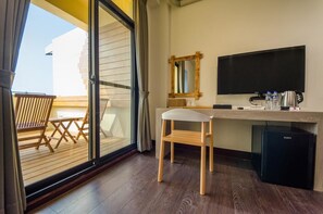 A hotel room with a sliding glass door leading to a balcony, a wooden desk with a chair, a television, and a minibar. - Anping 1923 Homestay (Tainan)