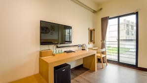 Ett modernt hotellrum med ett skrivbord i trä, en platt-TV, ett litet kylskåp, en stol och en stor skjutdörr i glas som leder ut till en balkong.
