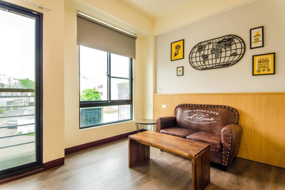 A modern room with a large window, a brown leather sofa, a wooden coffee table, and wall art including a world map and motivational quotes.