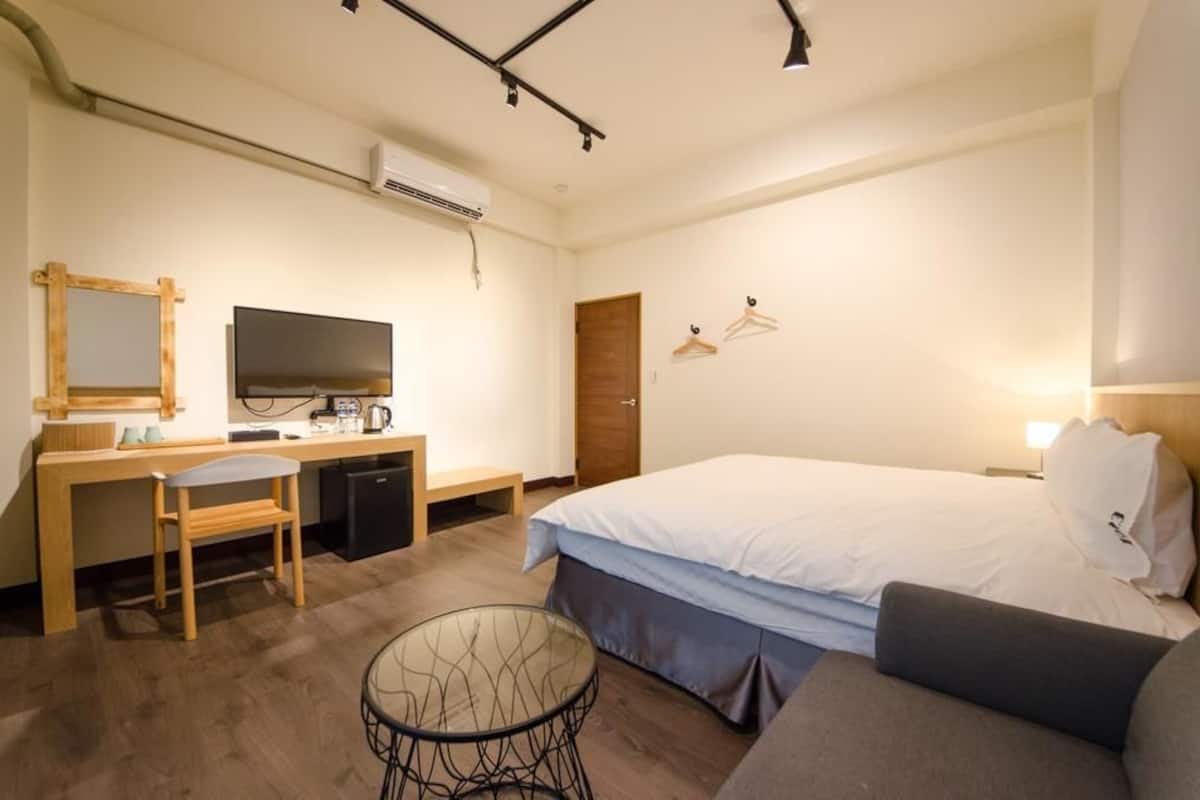A hotel room with a bed, a desk, a chair, a TV, a small table, and a wardrobe.