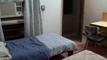 A room with two beds, a desk, a chair, and an air conditioning unit.
