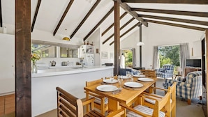 Amplia sala de estar con un comedor de madera para cuatro, una cocina con armarios blancos y un ventanal que ofrece vistas a zonas verdes.