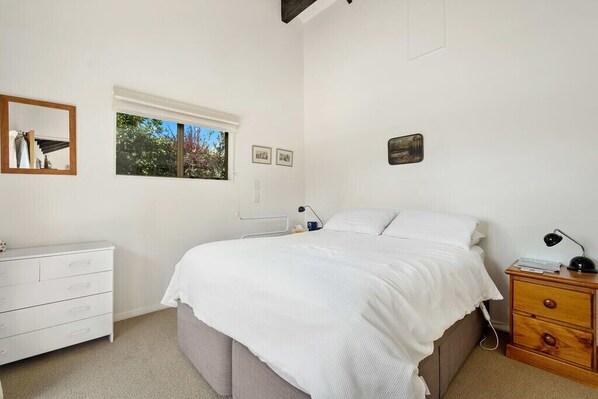 A bedroom with a bed, a bedside table, a dresser, a window, and wall decorations.