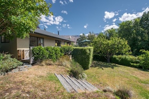 A house with a well-maintained lawn, a wooden deck, and a large tree in the backyard.