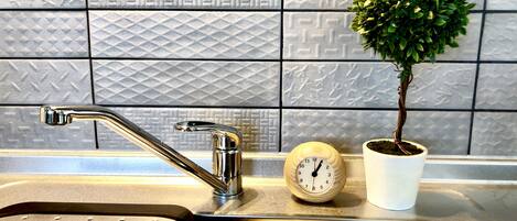 A kitchen sink with a modern faucet, a potted plant, and a wooden clock on the countertop.