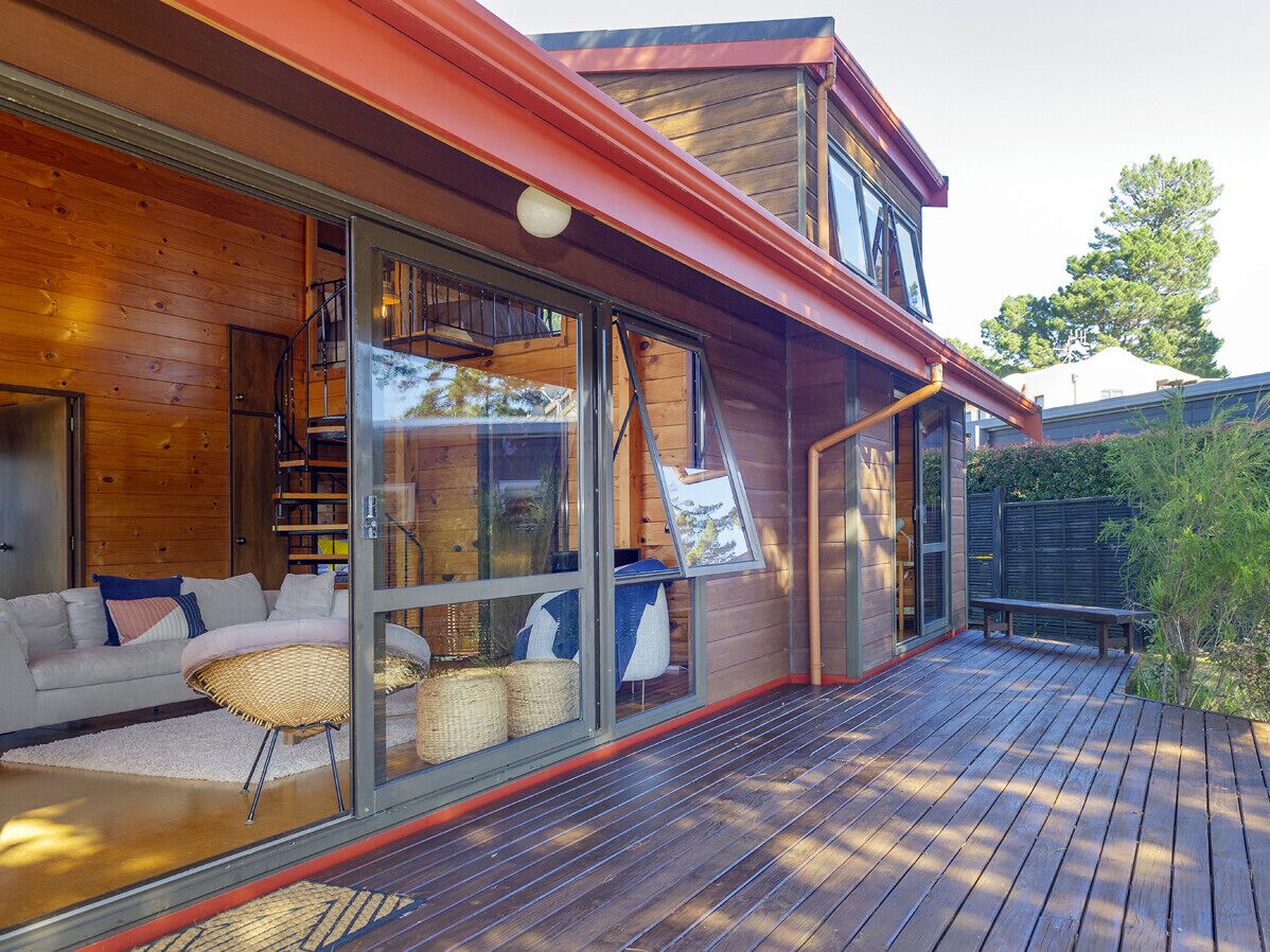 A modern wooden house with large glass windows, a deck, and a sofa with cushions.