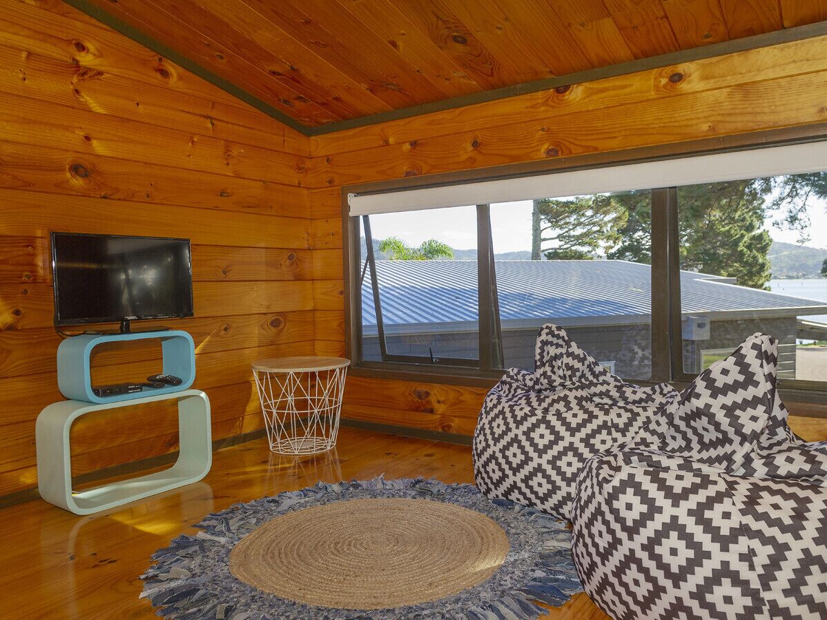 Een gezellig cabin interieur met een houten plafond, een televisie op een standaard, een geweven vloerkleed en een gestreept sofa.
