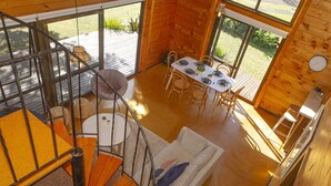 Uma cabana de madeira com área de jantar, escada e vista para o exterior.