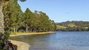 Vista para um lago com uma praia de areia, árvores densas e colinas ao fundo.