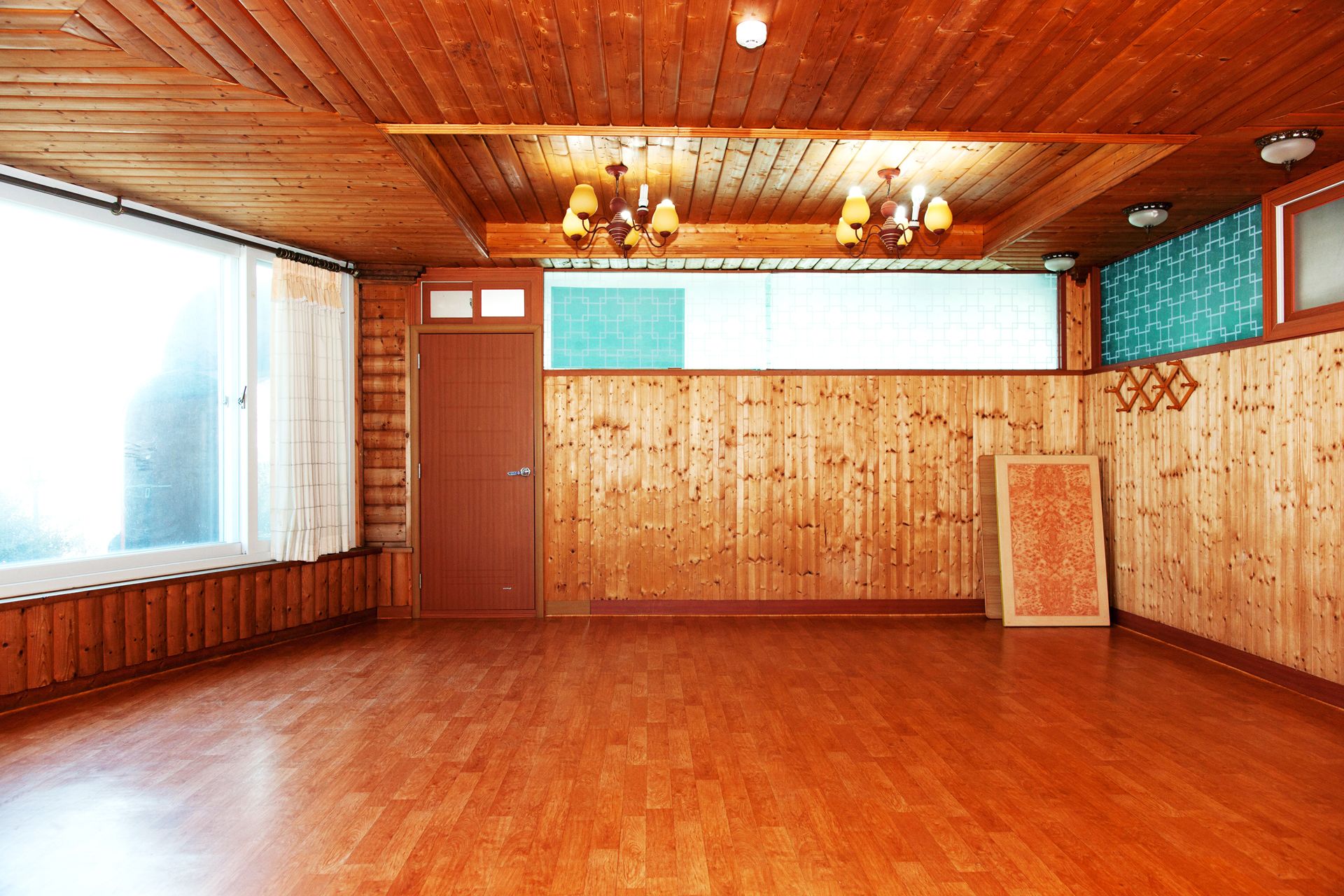 A room with wooden walls and ceiling, a large window, and a door.