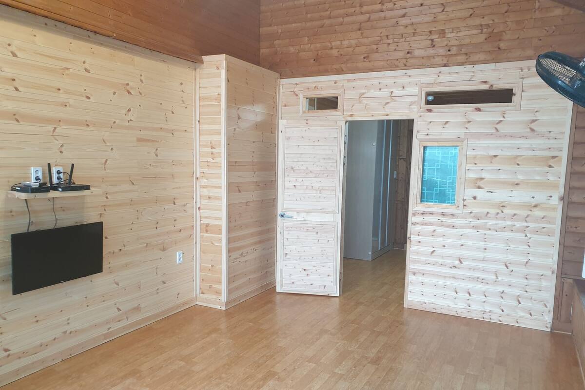 Huoneessa on puupaneloidut seinät, seinälle asennettu taulutelevisio ja puulattia.