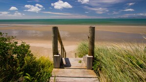 Un sentier en bois mène à une plage d’où l’on a une vue dégagée sur l’océan et le ciel.