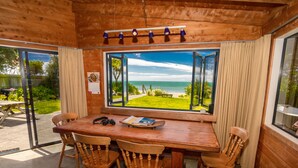 Un coin repas en bois, avec une table et des chaises, une fenêtre donnant sur la mer et un plafond orné de luminaires suspendus.