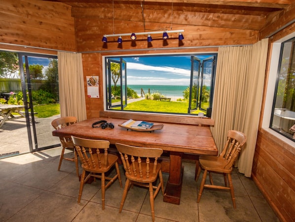 Uma área de refeições de madeira com uma mesa e cadeiras, uma janela com vista para o mar e um teto com luminárias pendentes.