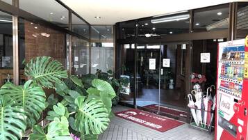 A modern hotel entrance with glass doors, a Coca-Cola vending machine, and a welcome mat.