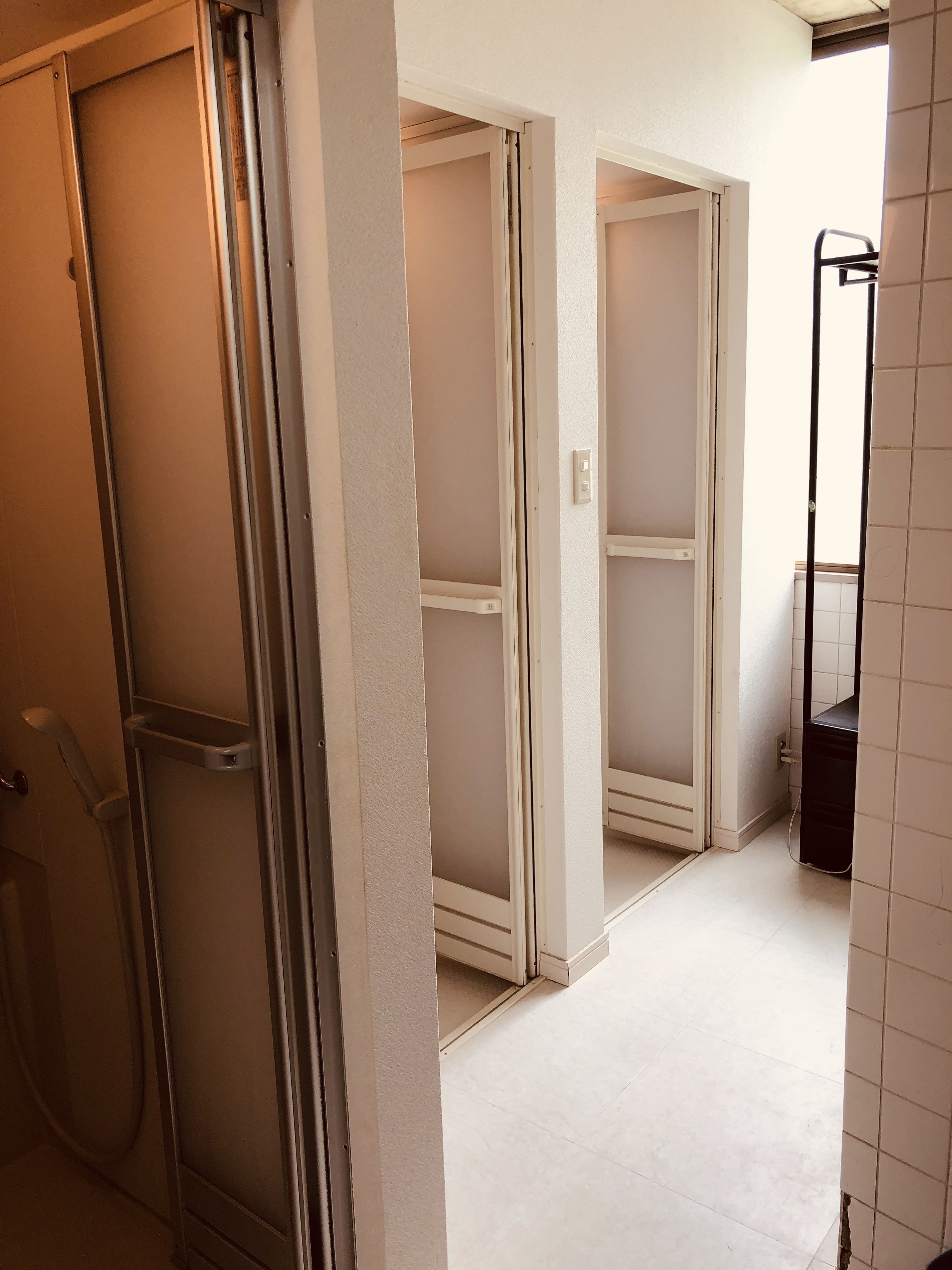 Un pasillo con un área de ducha a la izquierda, una puerta con perchero y una pared con azulejos a la derecha.