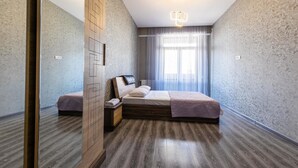 A bedroom with a wooden floor, a bed with a headboard, a nightstand, and a wall-mounted light fixture. - Apartment on Saakadze Square (Tbilisi)